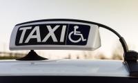 Et skilt på toppen af en bil. På skiltet ses teksten "Taxi" og et lille piktogram af en person i kørestol.