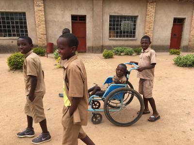Fem børn går sammen på en vej i Rwanda, et af børnene sidder i en kørestol og skubbes af et af de andre børn