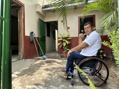 Alberto, mand fra Honduras, sidder i kørestol i en lille gårdhave og kigger alvorligt ind i kameraet.