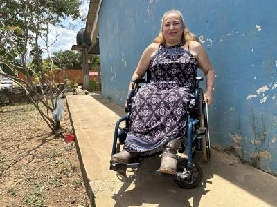 Fredesvinda, en kvinde fra Honduras. Smiler, i lang blomstret kjole. Sidder i sin kørestol udendørs foran en blå væg.