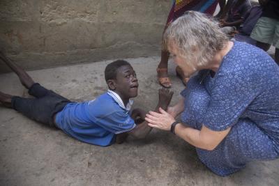 Anni Sørensen med en ung mand, der ligger på jorden ude foran familiens hus i Ghana