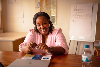 Rose, forpersonen for rwandas organisation for psykiatribrugere, sidder foran sit skrivebord i nydelig lyserød kjole og et stort smil.