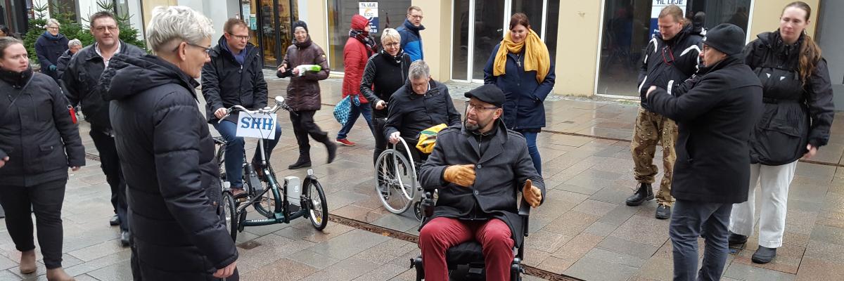 mennesker med handicap i sønderborgs gågade til handicapdag. de er i kørestol og på ben sammen med politikere.