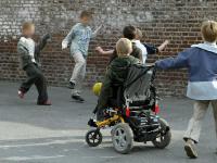 En gruppe af skolebørn spiller bold i skolegården. Et af børnene er i kørestol.
