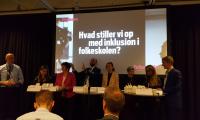 En række paneldeltagere sidder foran et billede med teksten "Hvad stiller vi op med inklusion i folkeskolen?"