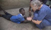 Anni Sørensen med en ung mand, der ligger på jorden ude foran familiens hus i Ghana