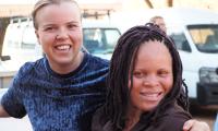 En ung dansk kvinde holder smilende om skulderen på en ugandisk kvinde med albinisme