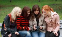 Fire teenagepiger sidder sammen på en bæk og kigger på et spejlreflekskamera