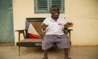 Johnnie Gyamfi Yeboah sidder på en bænk foran et hus og fortæller